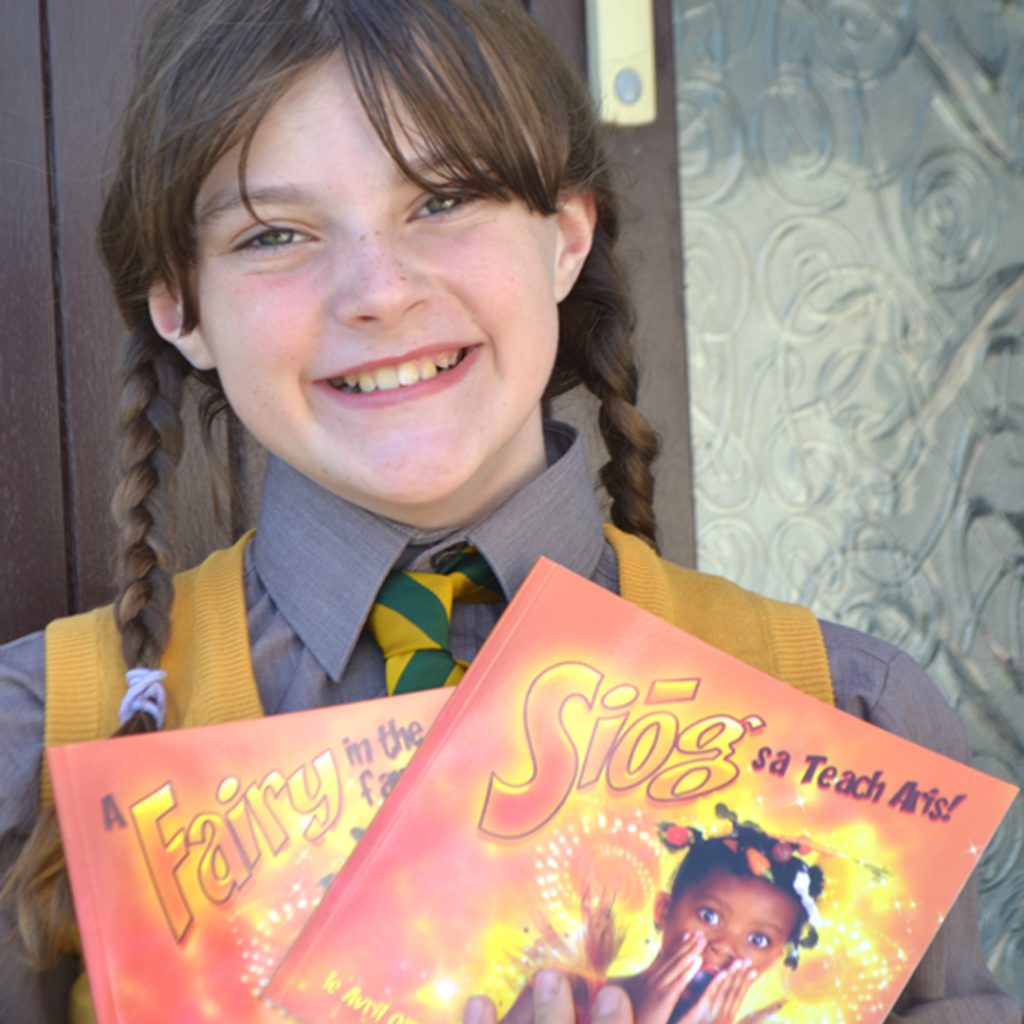 A girl in school shirt and tie holds her dual language English and Irish book