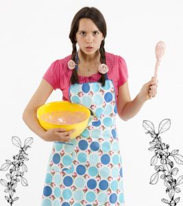 Angry girl in rose patterned apron waving a wooden spoon