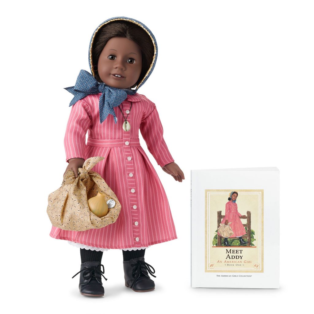 Smling black doll in historic costume next to her storybook