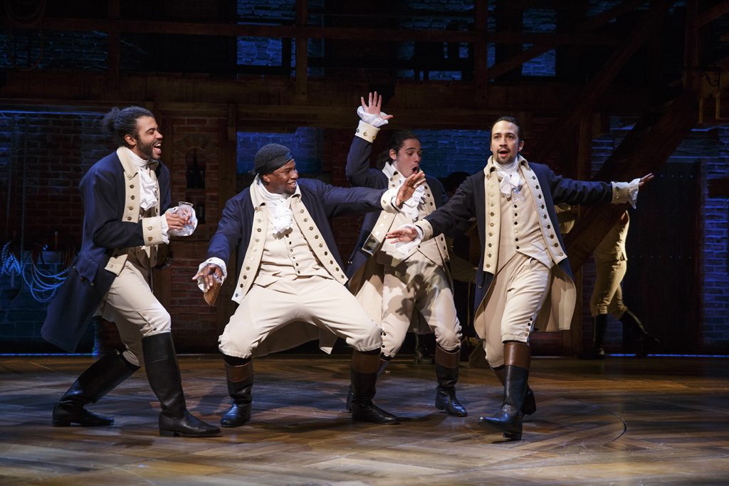 Four actors in historical costume dancing onstage in the musical Hamilton