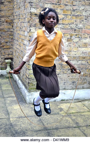 Little black girl in school uniform skipping beside a brick wall