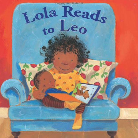 a little girl with an afro hairstyle reads to her baby brother who is on her lap