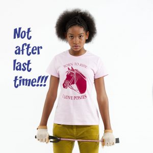 A teenage girl in jodhpurs and horsey t-shirt holds her riding crop in a defensive pose