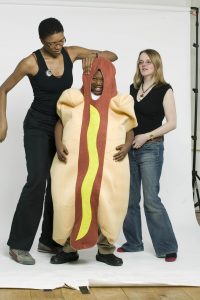 A boy in a hot dog costume is helped by two women